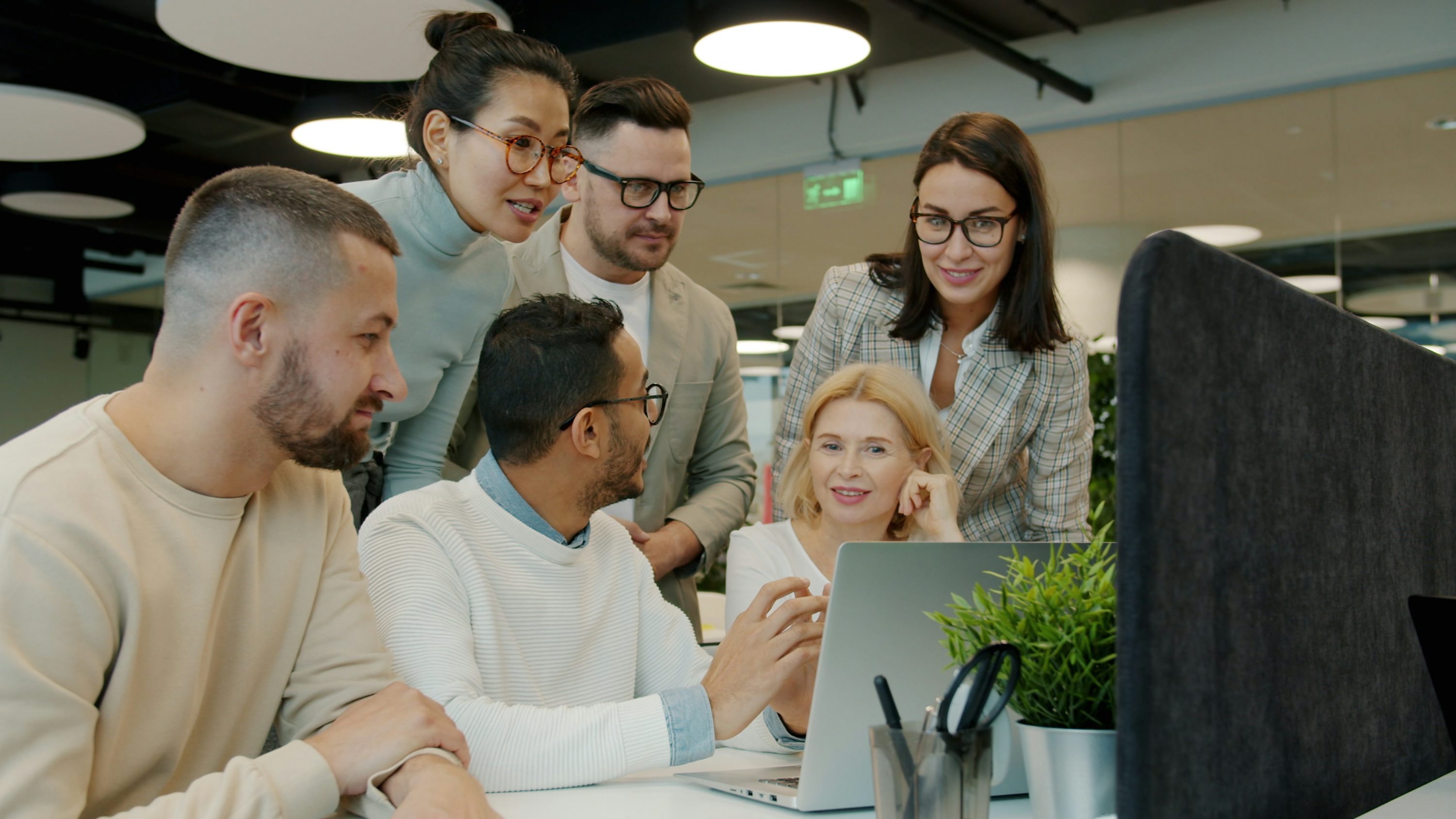 A diverse professional team collaborating around a laptop in a modern office